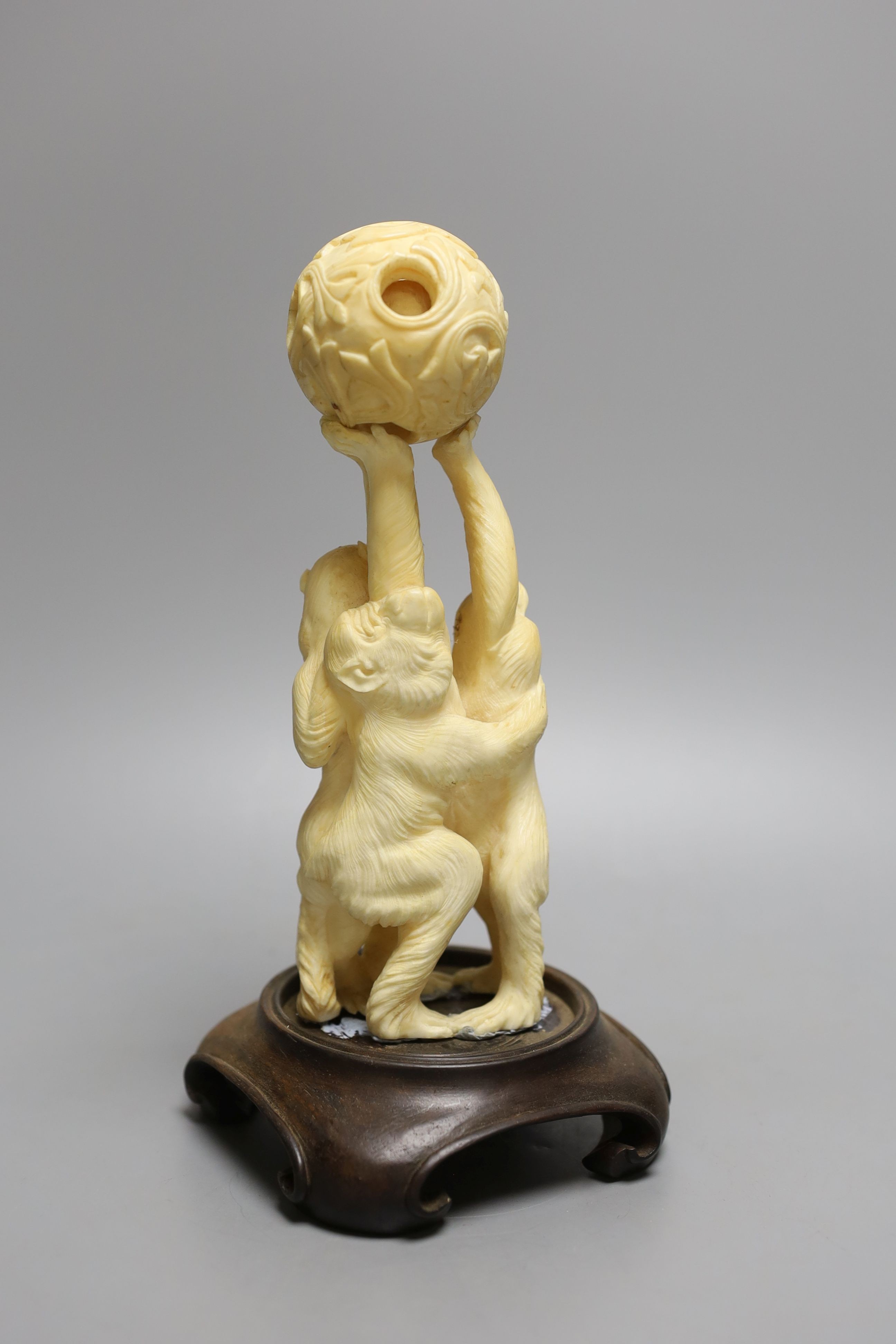 A Japanese ivory okimono of the three wise monkeys supporting a puzzle ball, early 20th century, wood stand, 20.5cm tall